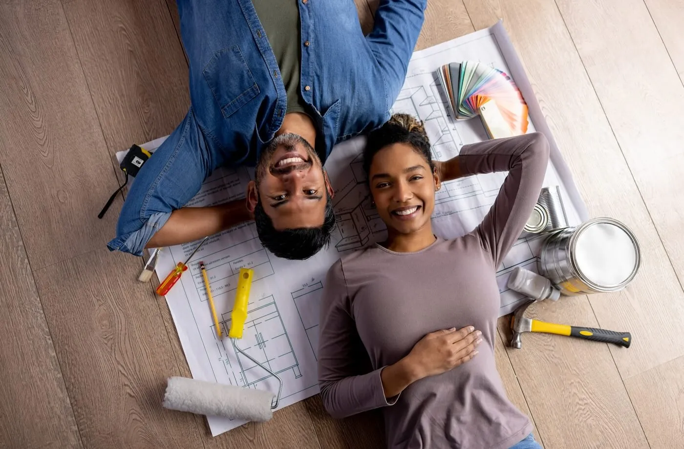 Happy couple lying on the floor on the draft sheet surrounded by renovation tools