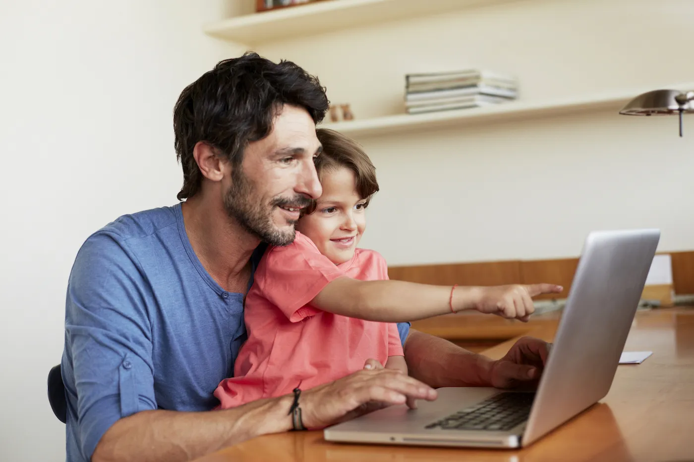 Happy father and son using laptop together at table in house