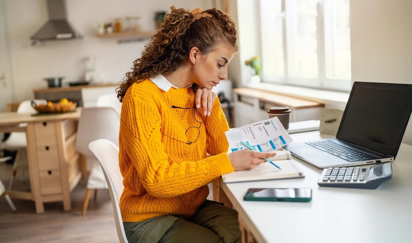 Woman reviewing escrow payment printouts while sitting at her desk with a laptop