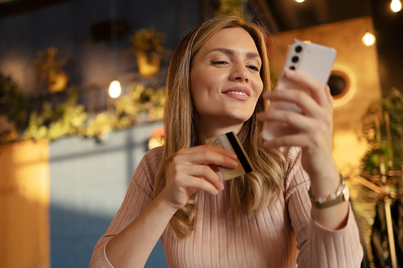 Young Woman Using Credit Card and Mobile Phone for Online Shopping in Coffee Shop.