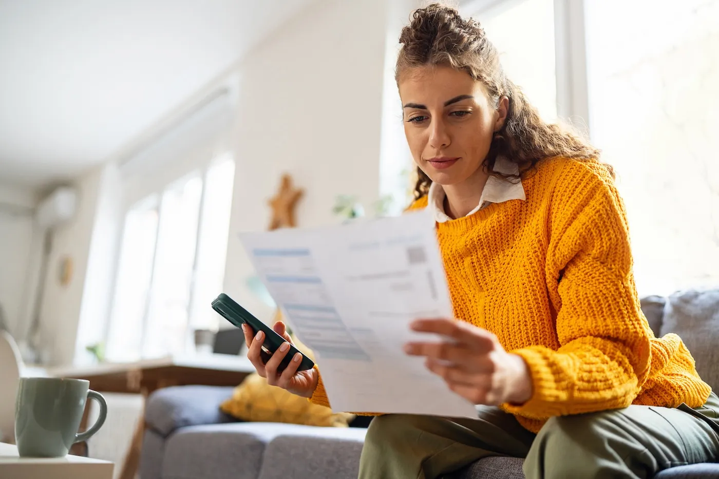 While organizing home finances, woman using mobile phone to calculate