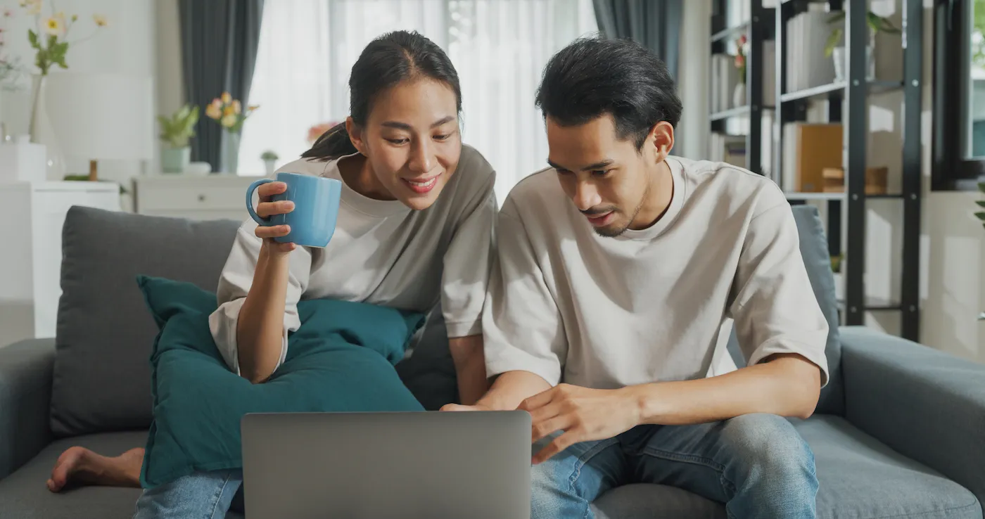 Happy young couple sitting on their couch using laptop computer