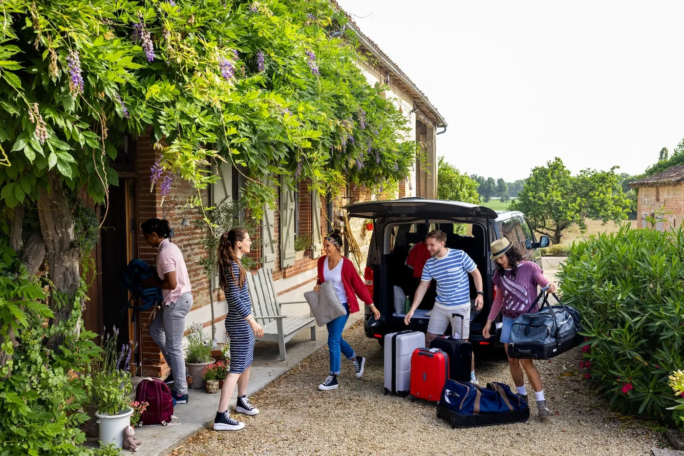 A small group of friends getting their luggage from the trunk of the minivan they have rented whilst holidaying in Toulouse in the South of France. They have arrived at their holiday villa on a bright summers day.