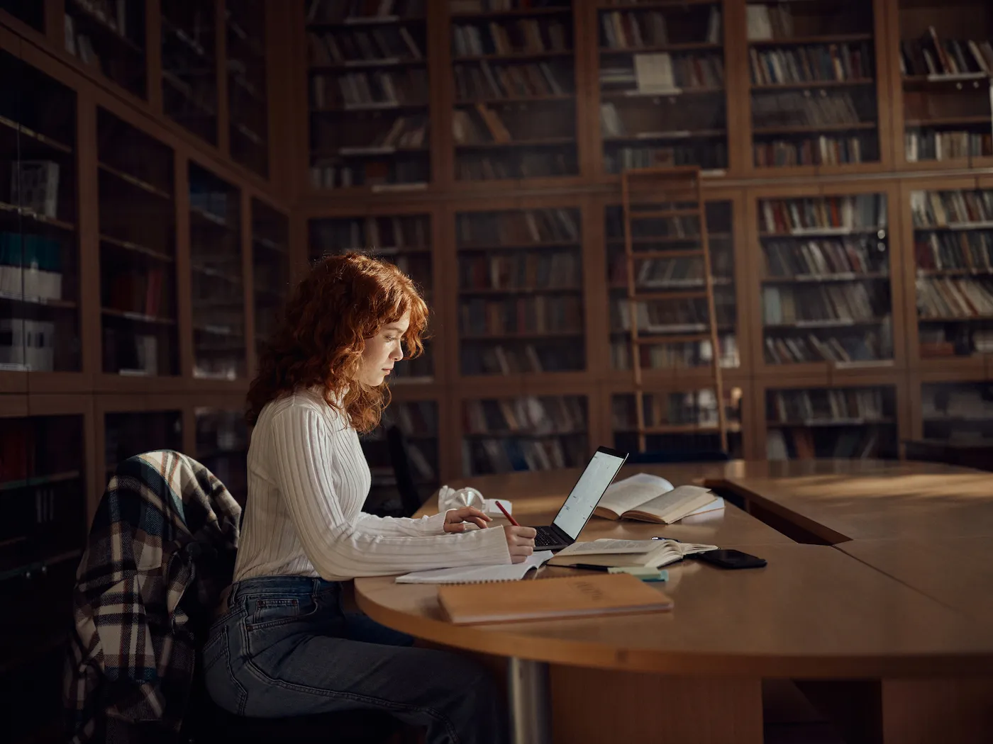 A female student taking notes while using a computer in library.