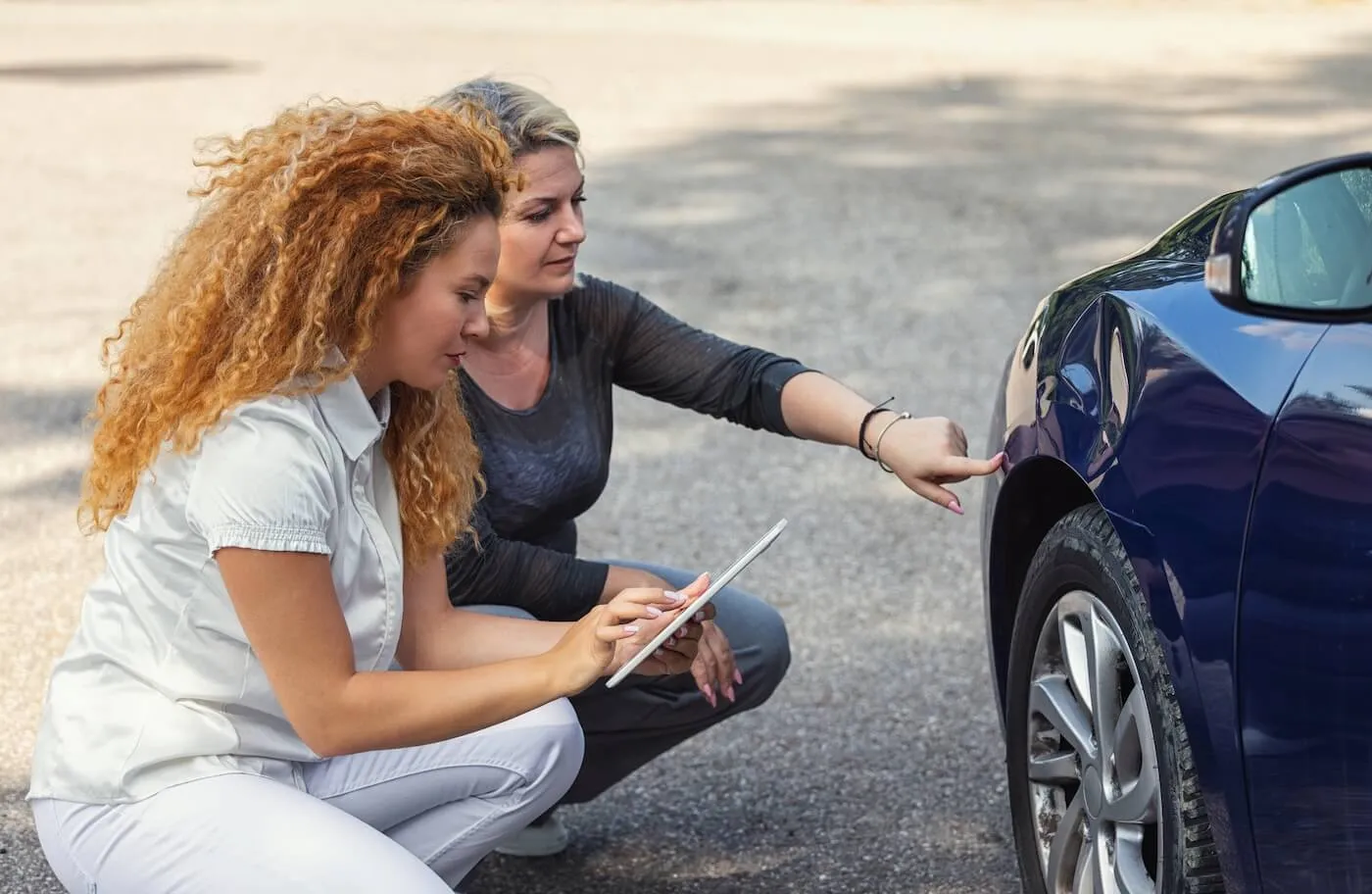 Two women inspecting the damage of the blue car after the accident