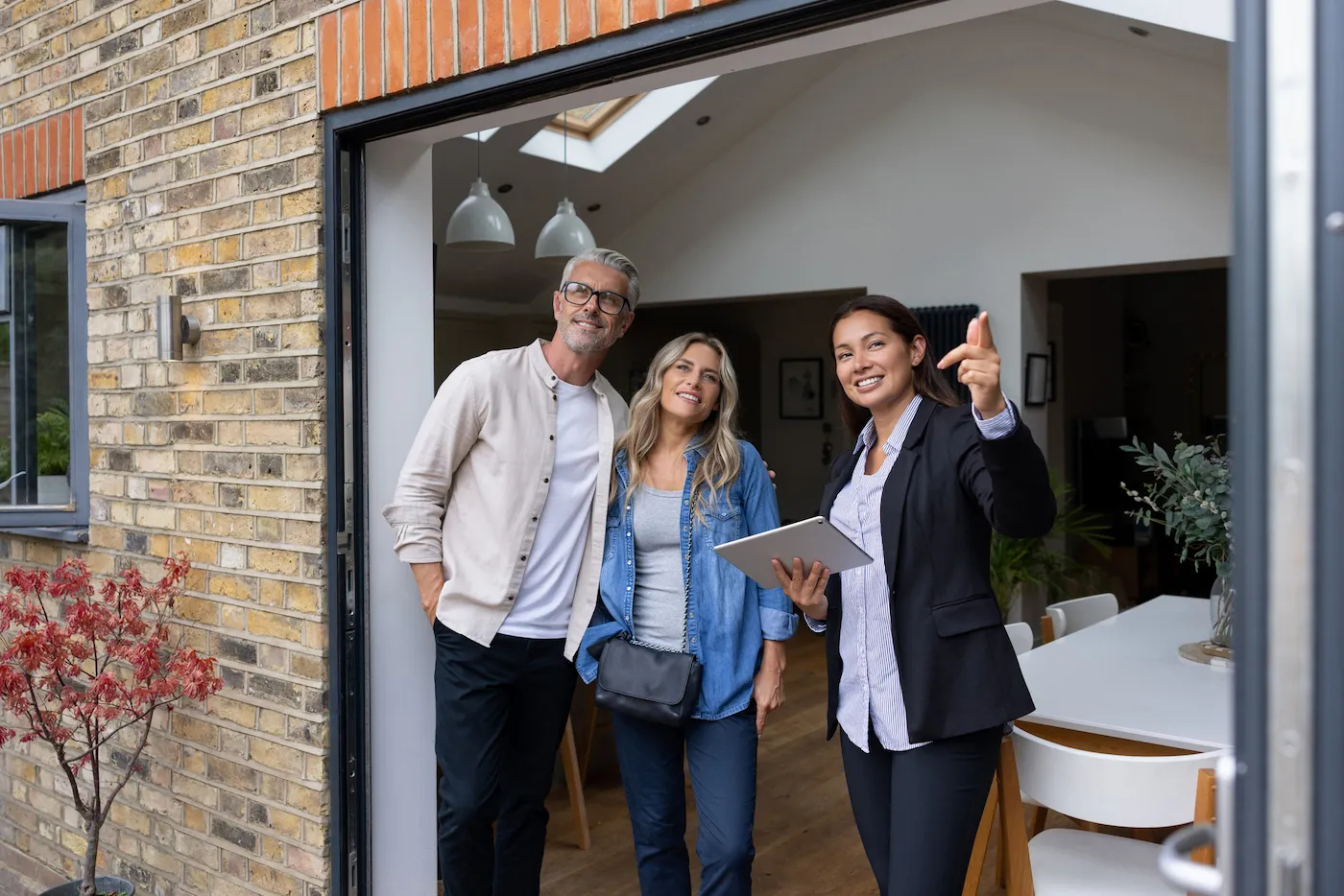 Real estate agent showing a house for sale to a couple and pointing outside. The three of them are standing in a large doorway.