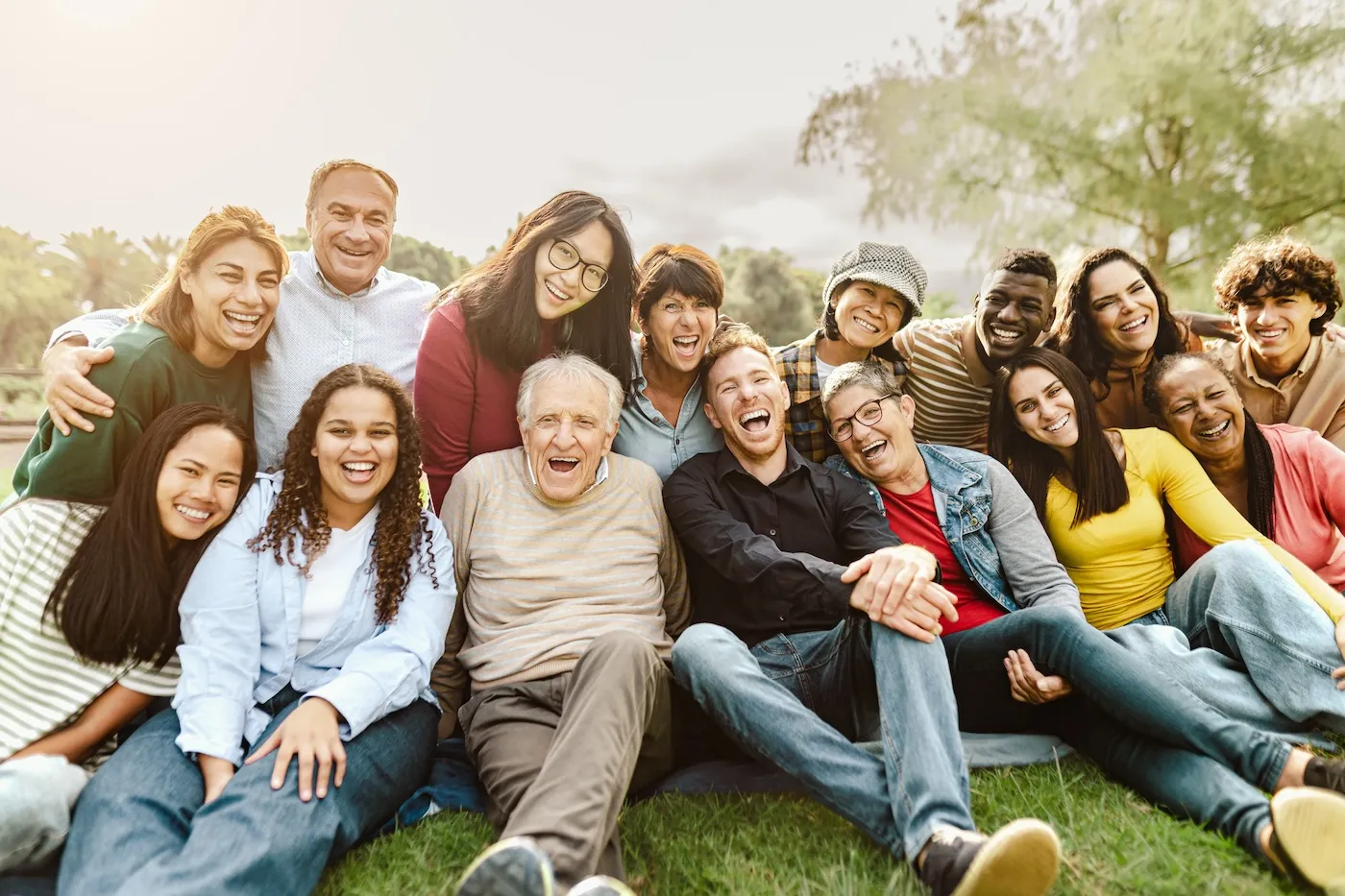 Happy multigenerational people having fun sitting on grass in a public park.