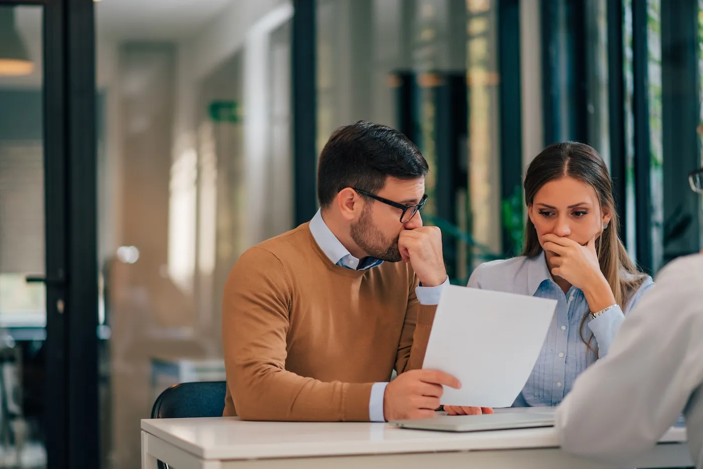 Portrait of a couple with financial problems looking at document in financial adviser's office.