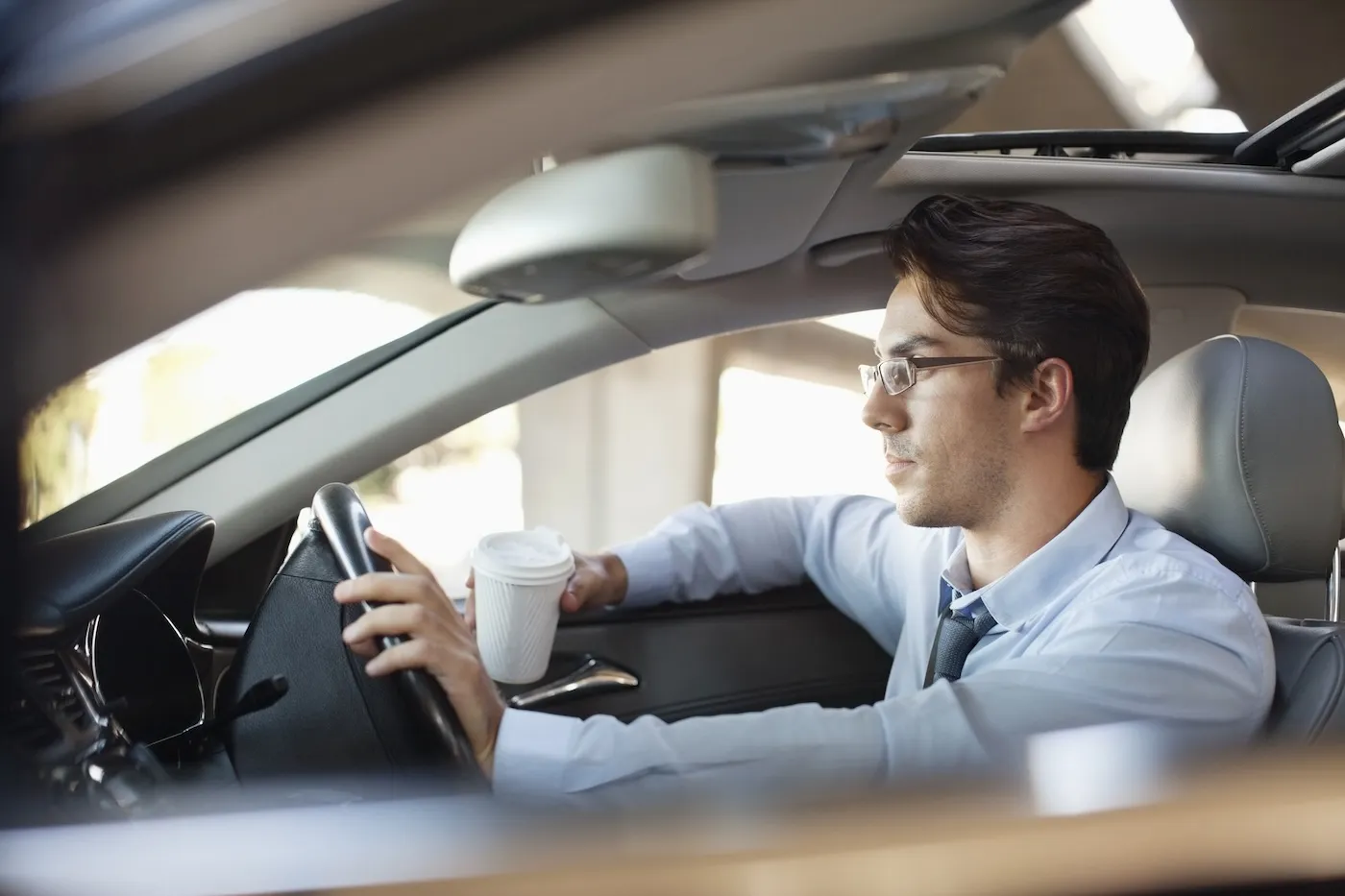 A man holding a coffee cup and driving his car.