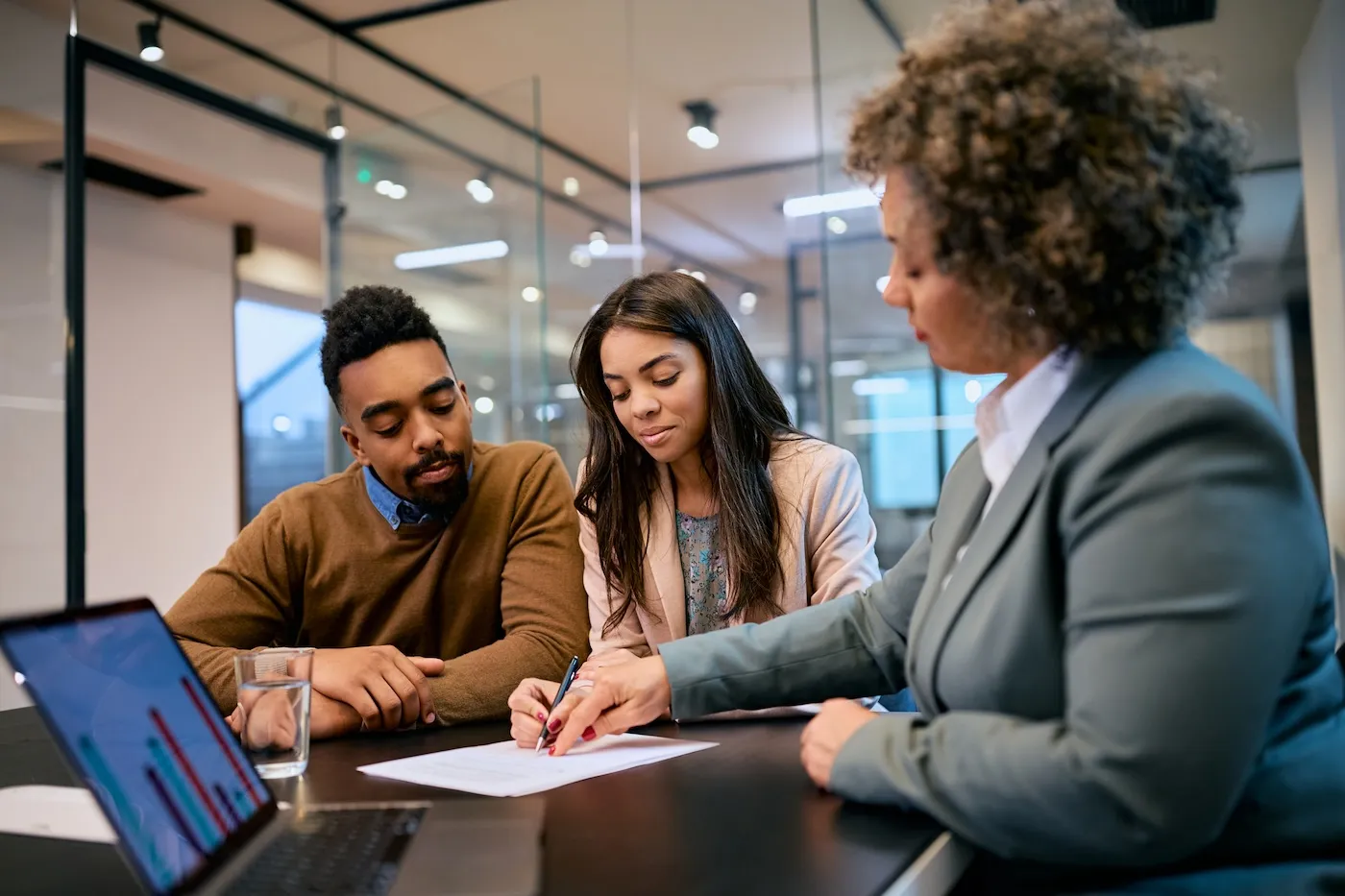 A woman and her husband signing mortgage agreement during a meeting with their bank manager.