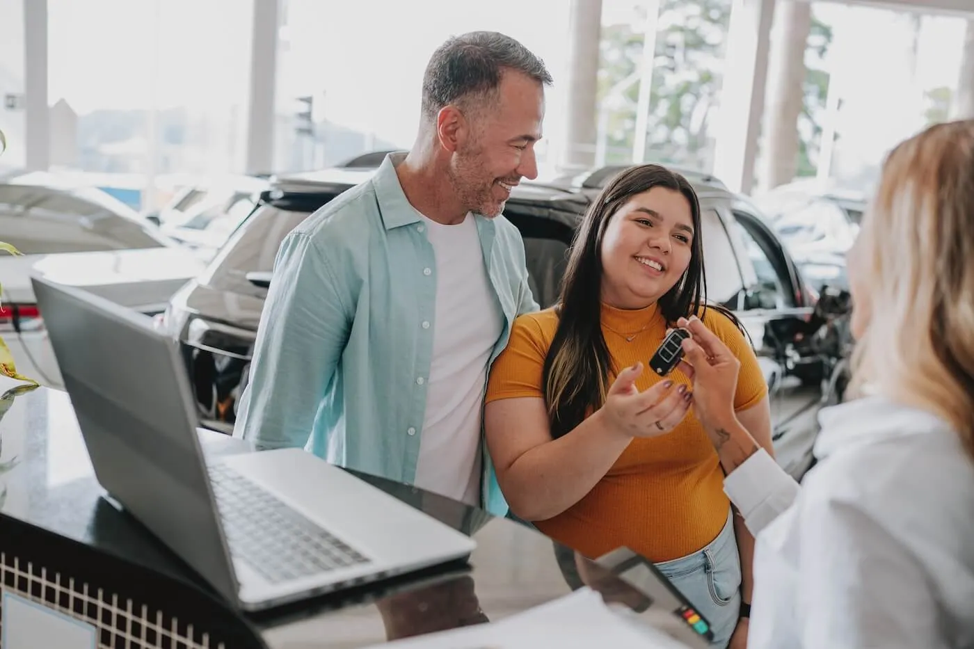 Smiling young woman and mature man receive the car keys from the dealership agent