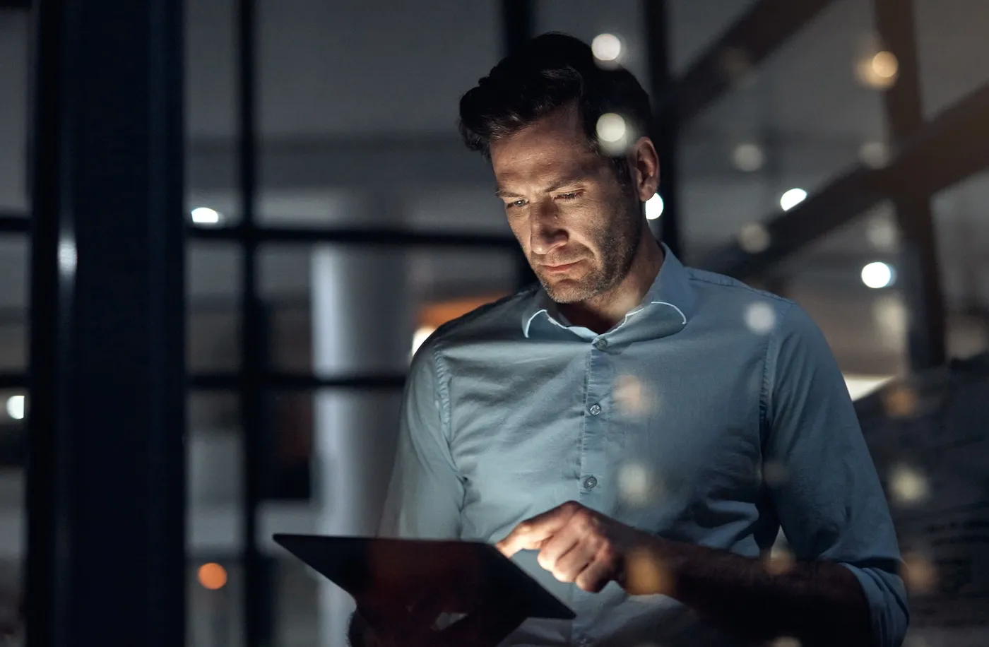 A man holding a tablet and working late at night while checking his credit score