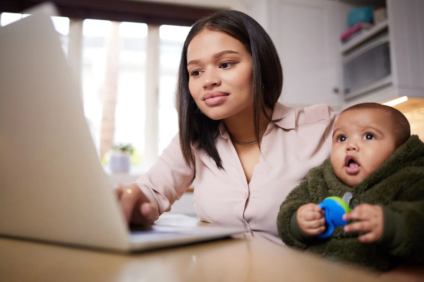 Shot of a young woman using a laptop while caring for her adorable baby at home