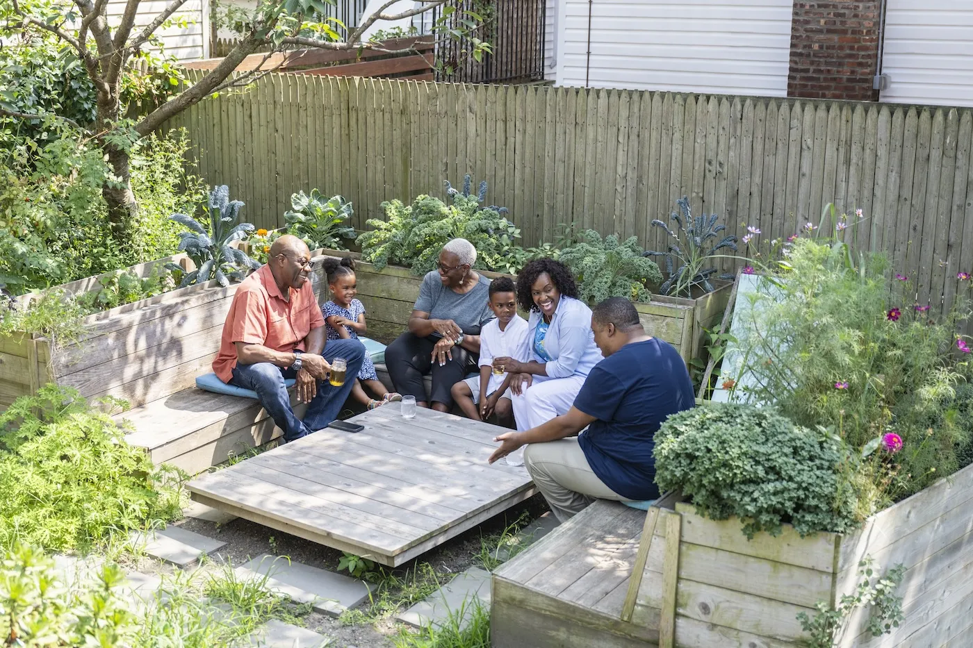 A multi-generational family sitting in beautiful green backyard sitting area, talking and laughing.