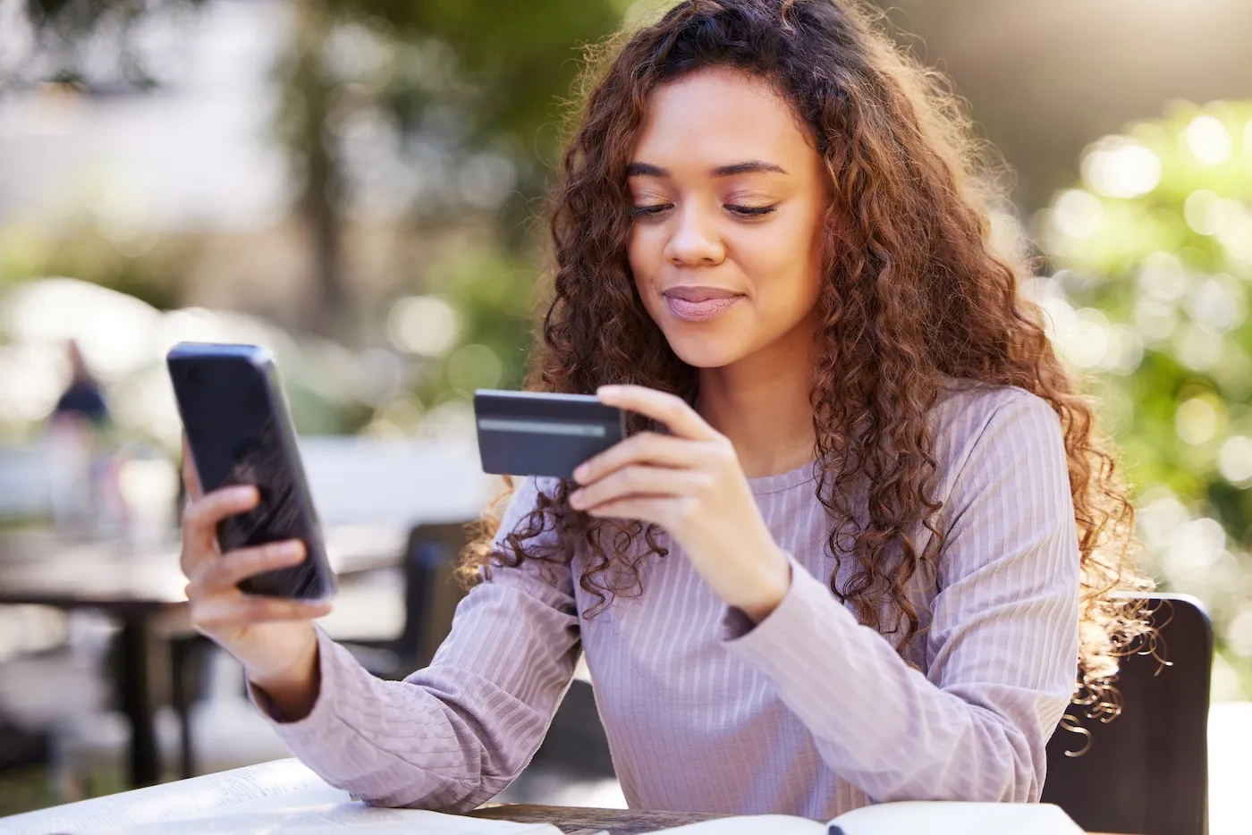 Shot of a young woman using a credit card and phone at a cafe.