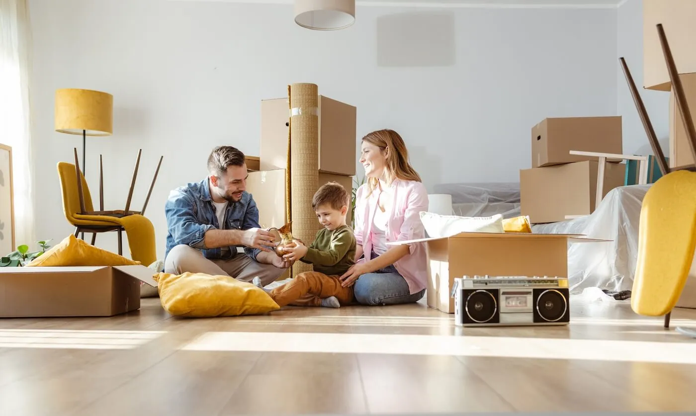 A family of three sitting on the floor in their new house surrounded by boxes