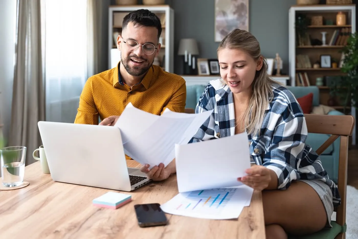 Young couple reviewing printouts and using a laptop on the coffee table in the living room