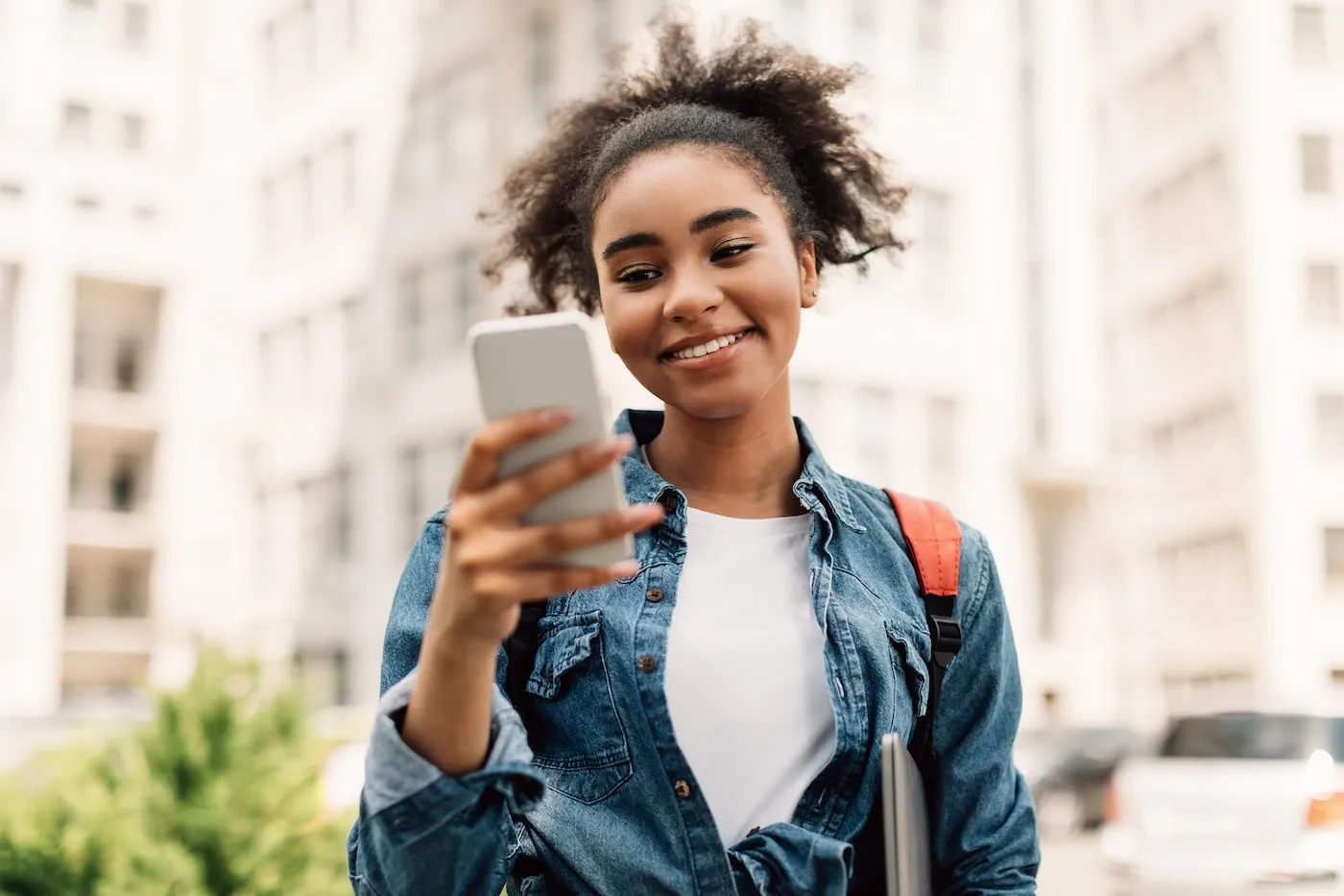 A woman standing outside in an urban environment using her mobile phone to check her credit card application.