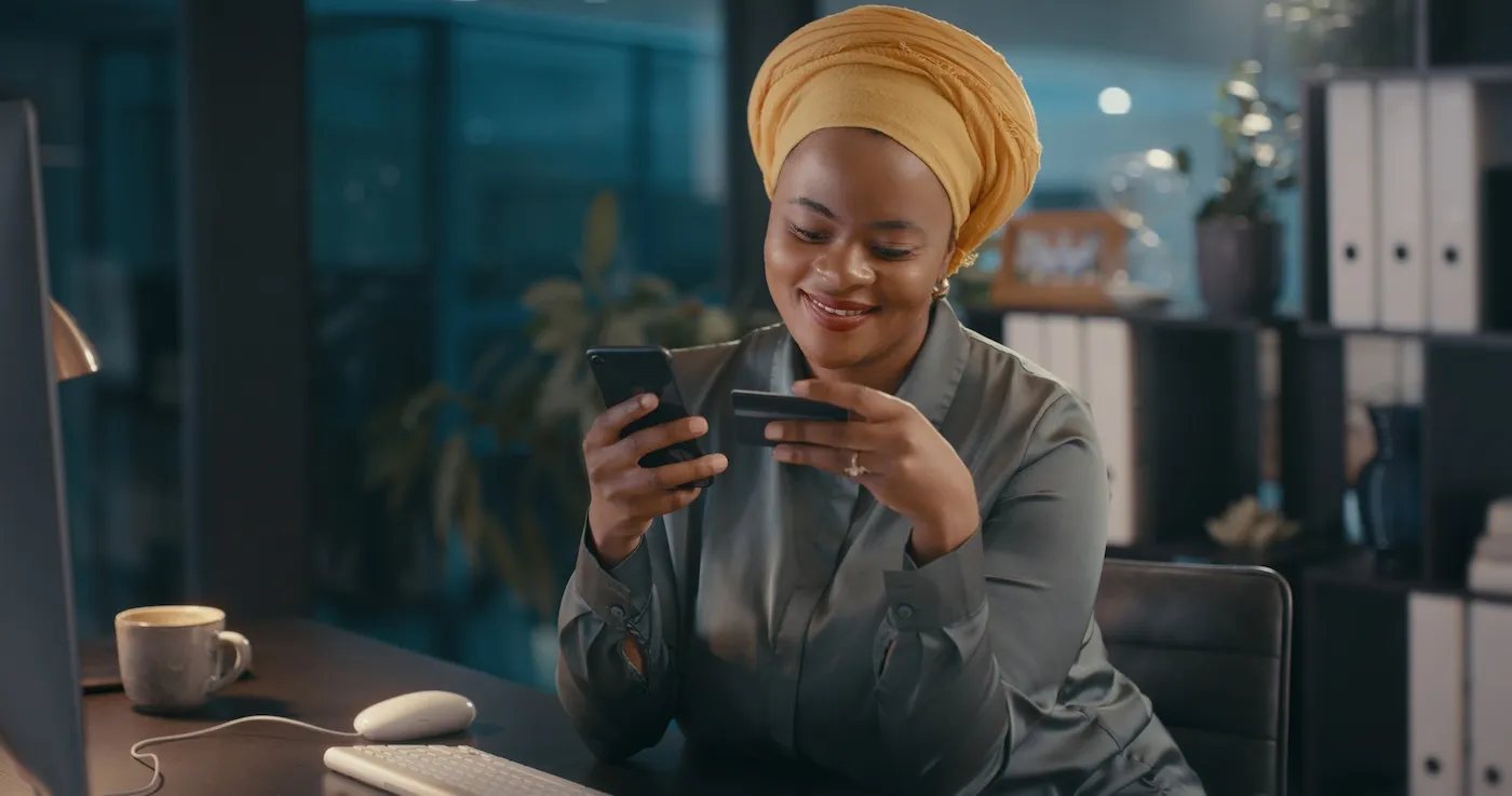 A woman holding her credit card and her phone, checking her card benefits online.