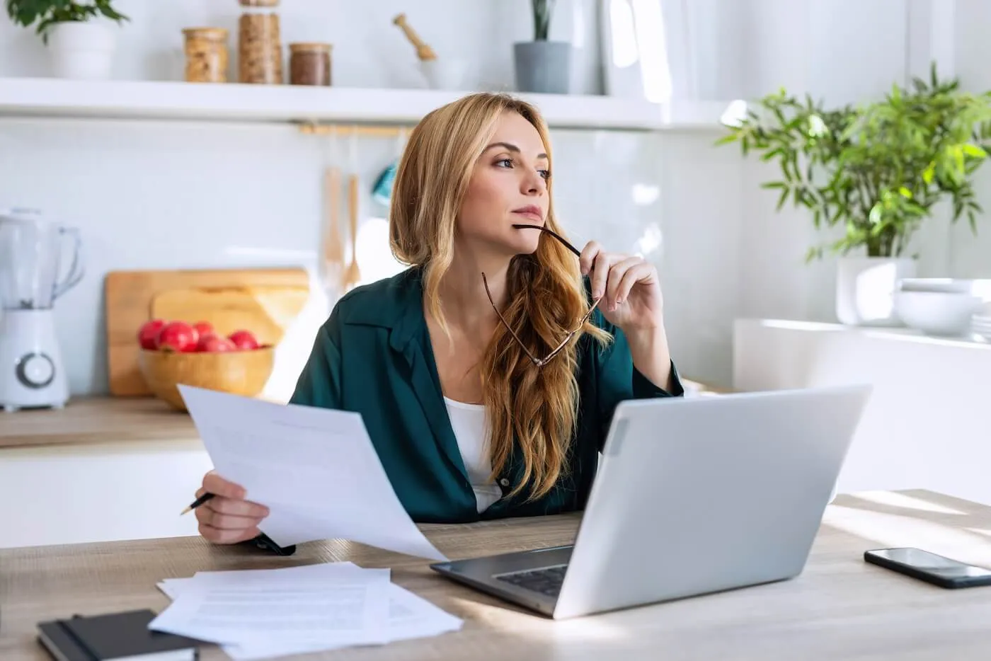 A woman holding her glasses and papers at her desk thinking about the best high-yeld savings account