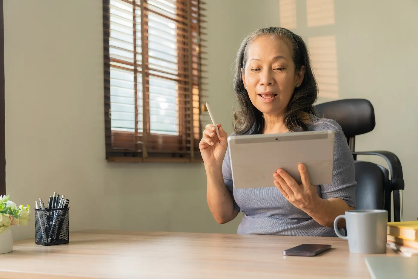 A woman sitting by the window and using portable digital tablet to surf the internet.