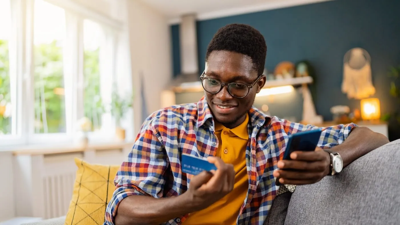 A smiling man holding a smartphone and a credit card