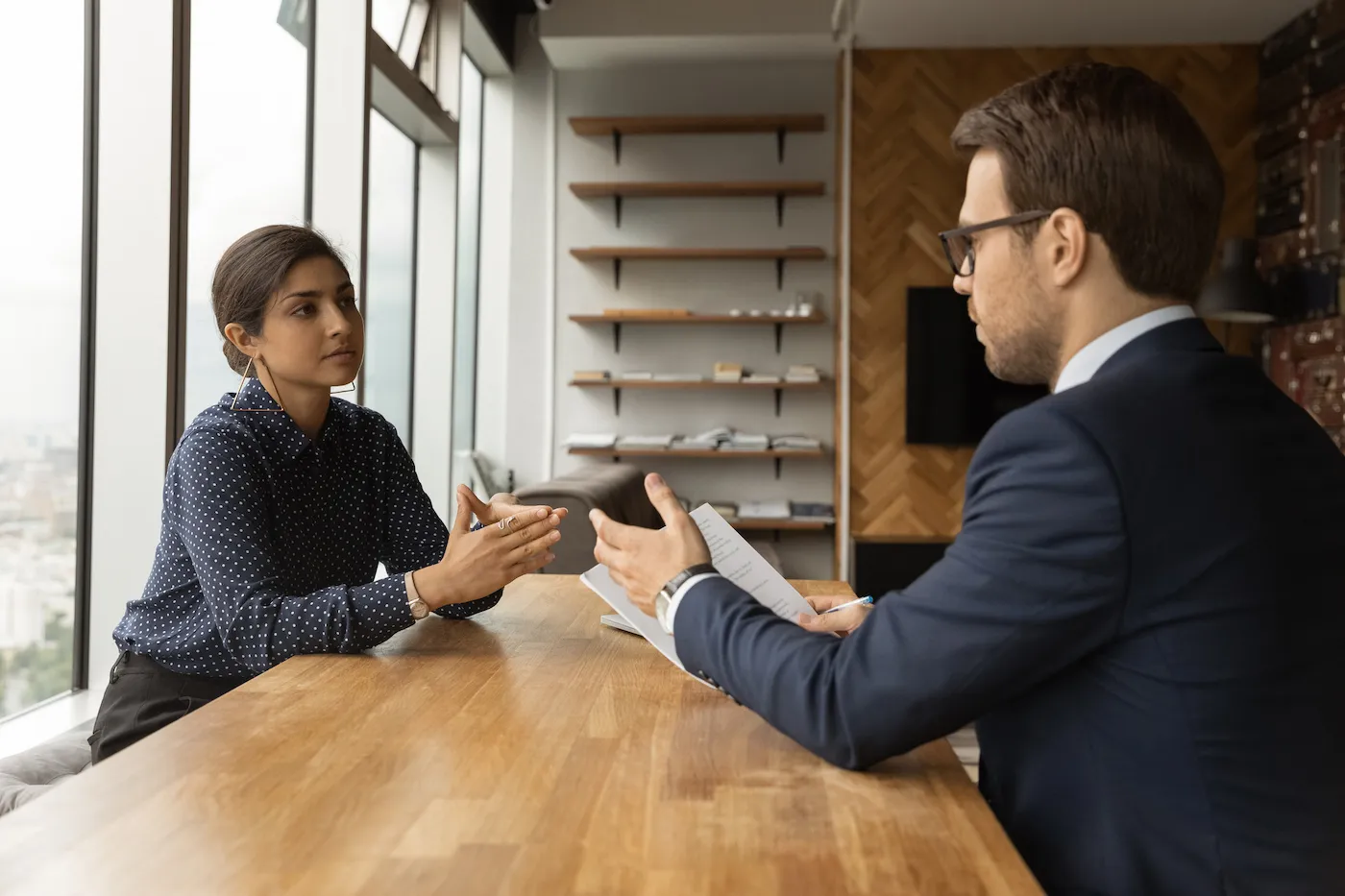 A woman sitting at a large wood table with her financial advisor as she fires him.