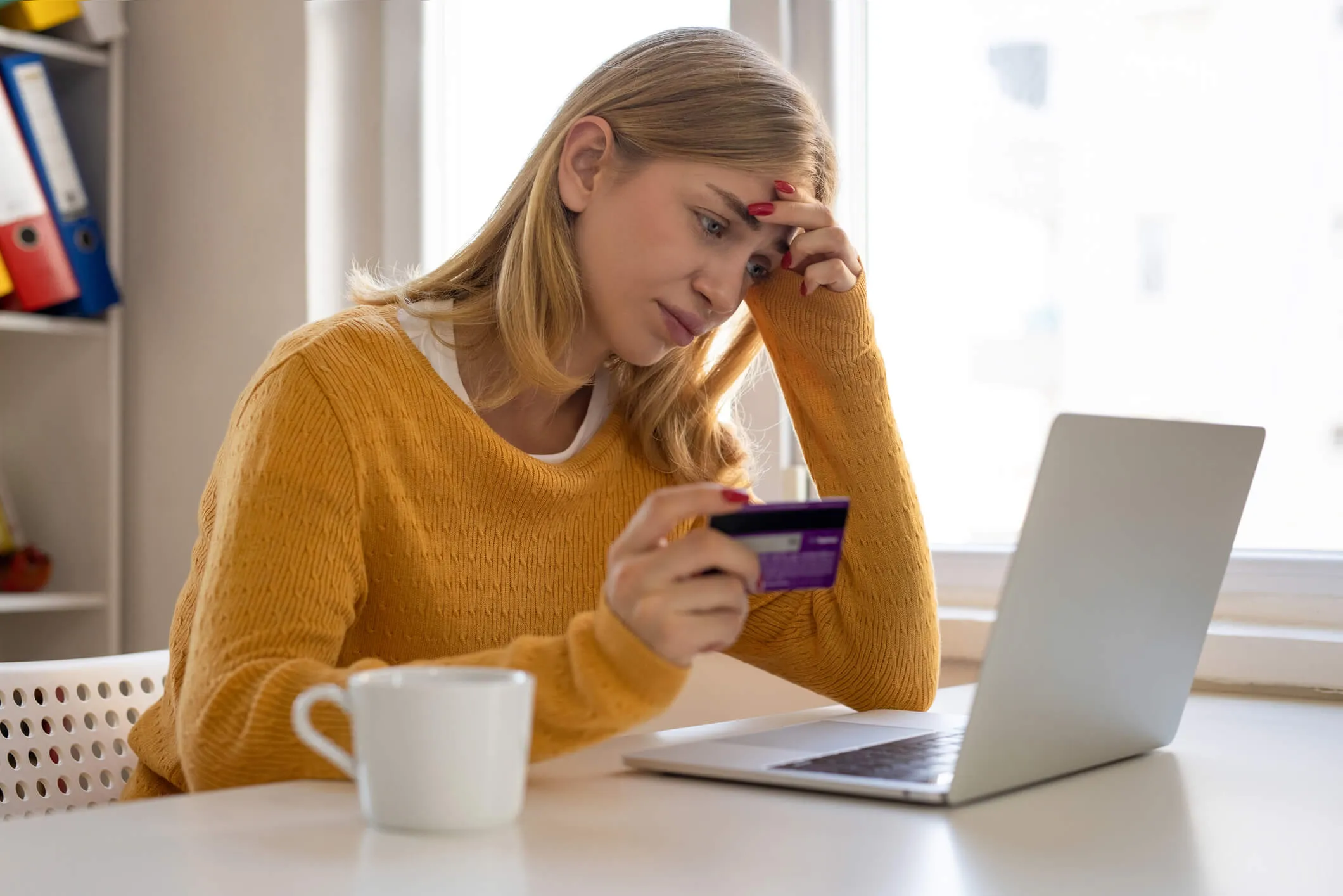 Concerned young woman holding a credit card while looking at laptop monitor