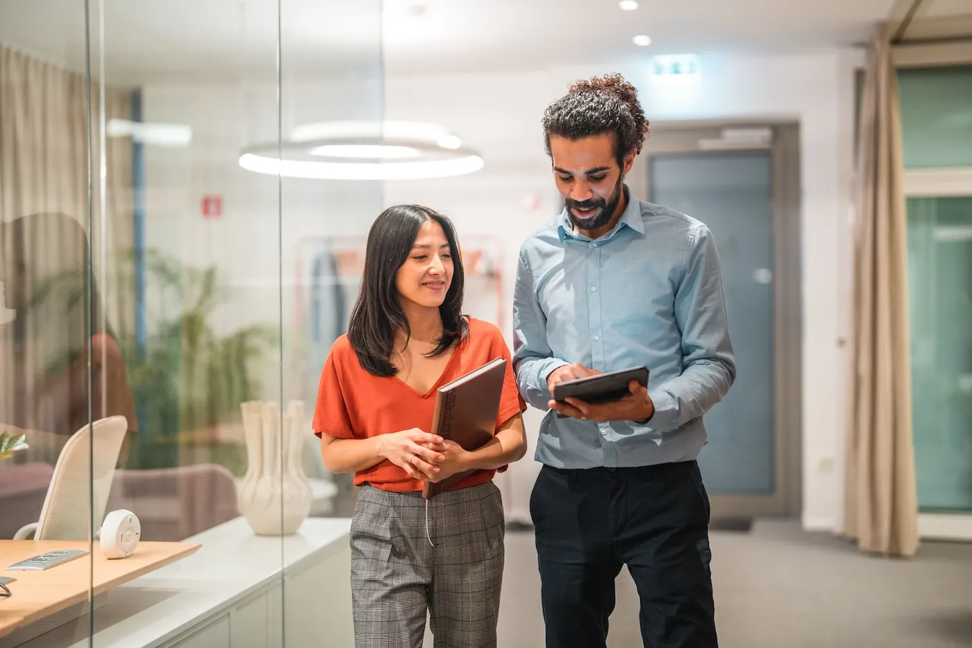 Two colleagues are seen engaging in a productive conversation while utilizing a digital tablet in a modern office setting.