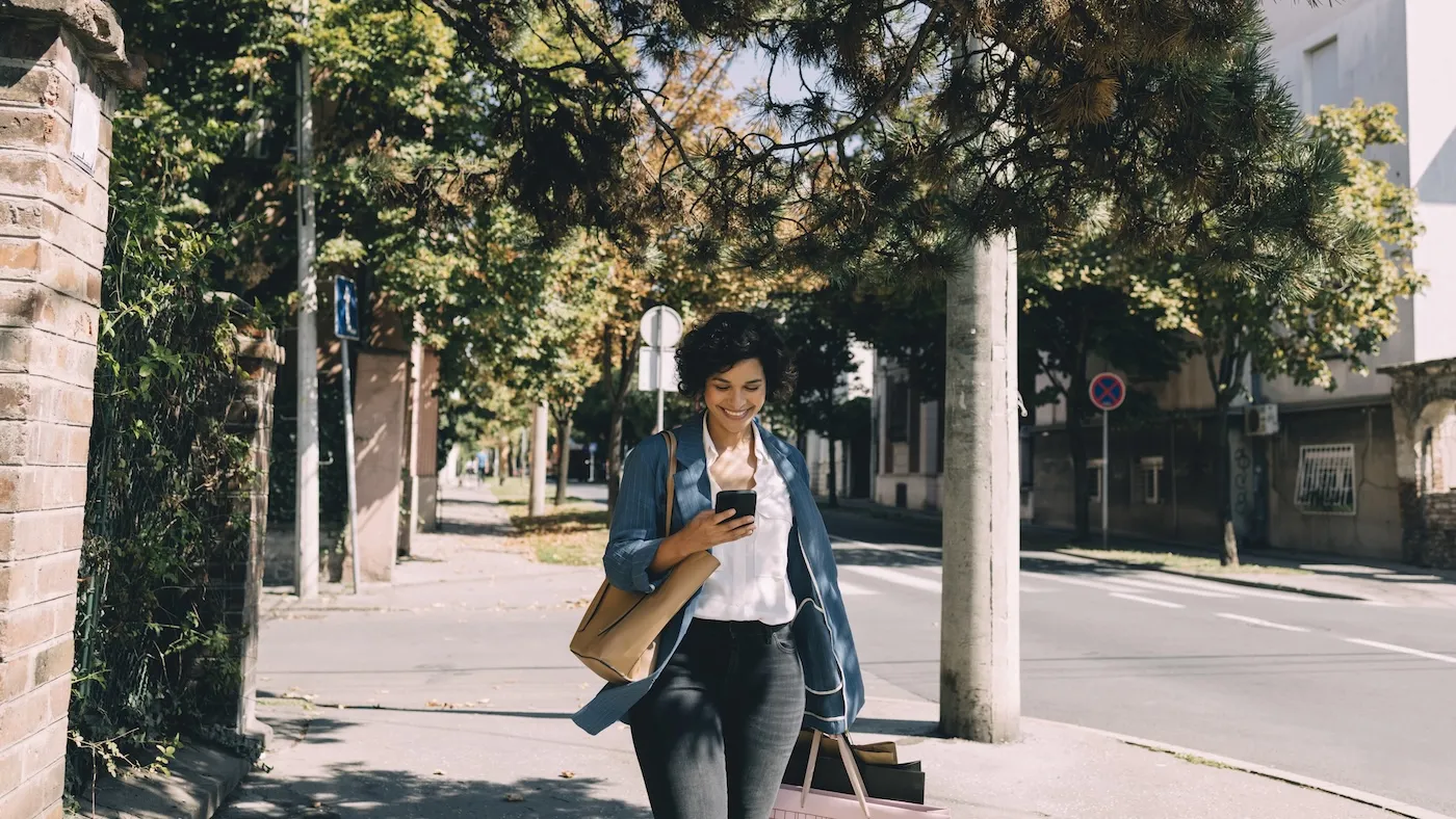 Smiling woman walking with shopping bags and looking at her smartphone.