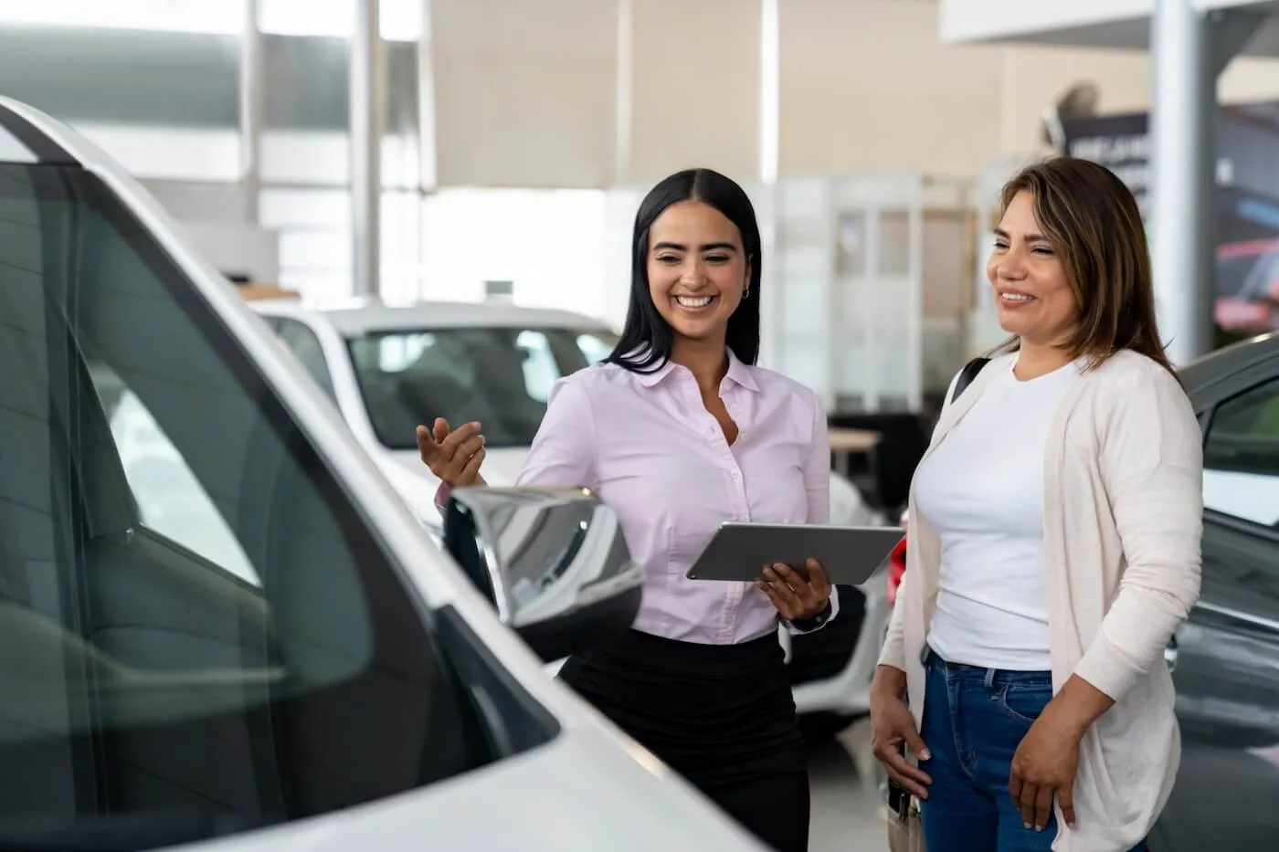 Mature woman shopping around in the car dealership while having a chat with the female agent