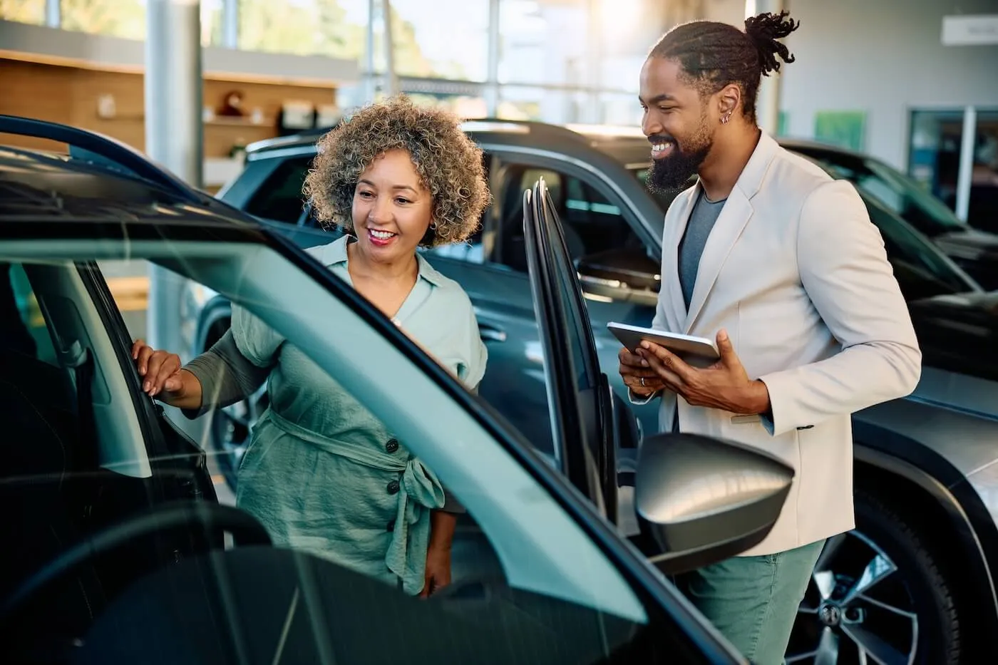 Smiling woman looking inside her new car while chatting with a male dealership agent