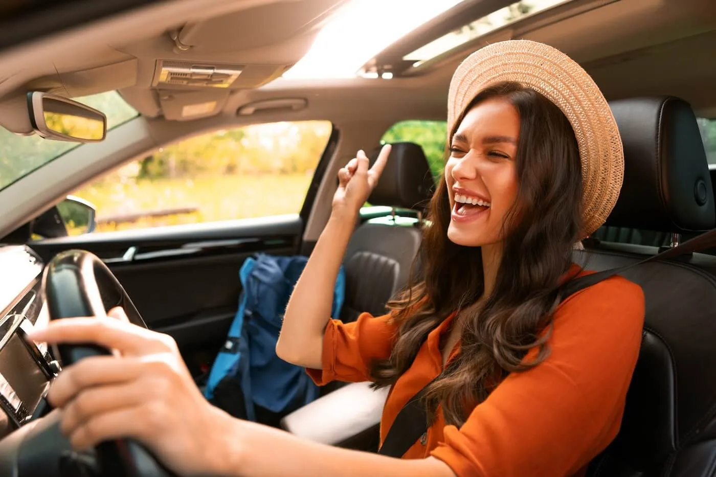 Happy young woman in a straw hat driving a car and singing