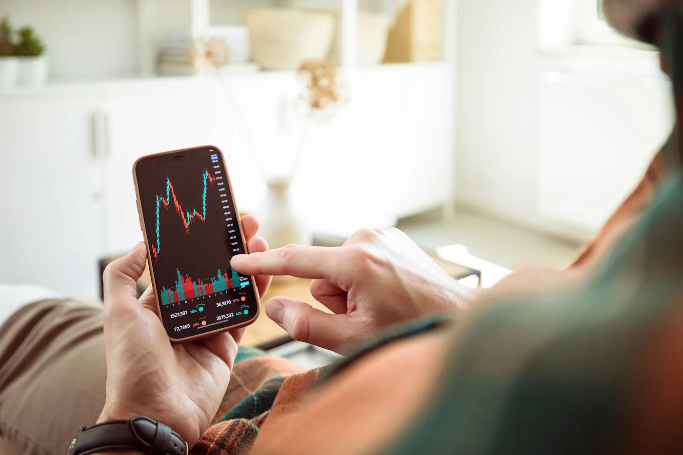 Man sitting on sofa at home and using smart phone, watching stock charts.