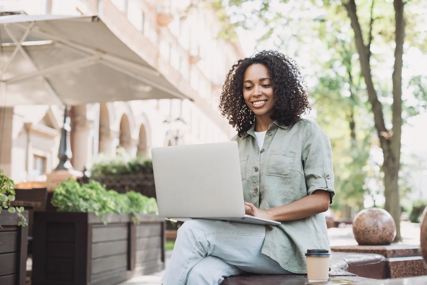 Smiling woman using her laptop computer outside in an urban outdoor area. She is opening a savings account online.