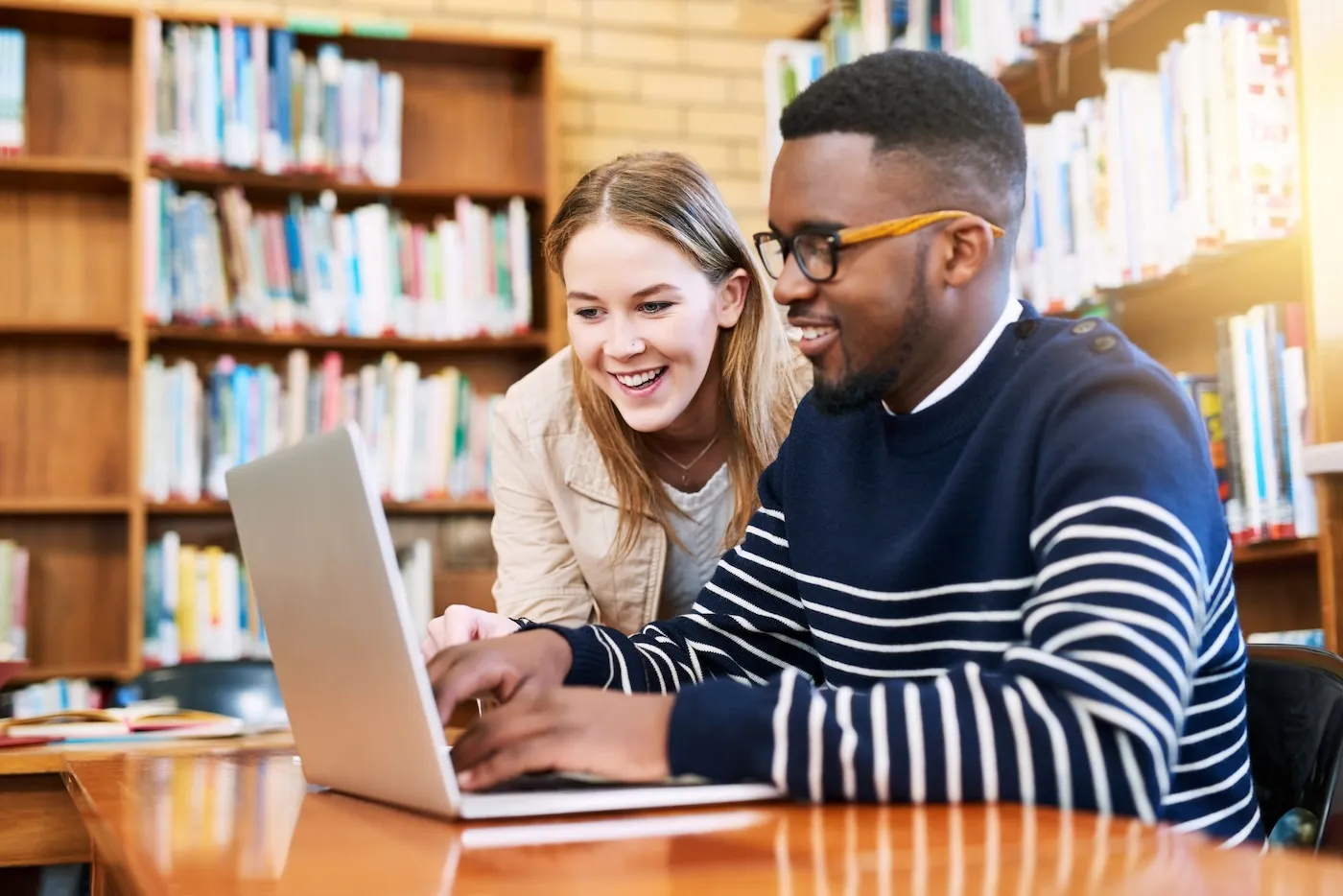 Shot of two people using a laptop in a library.