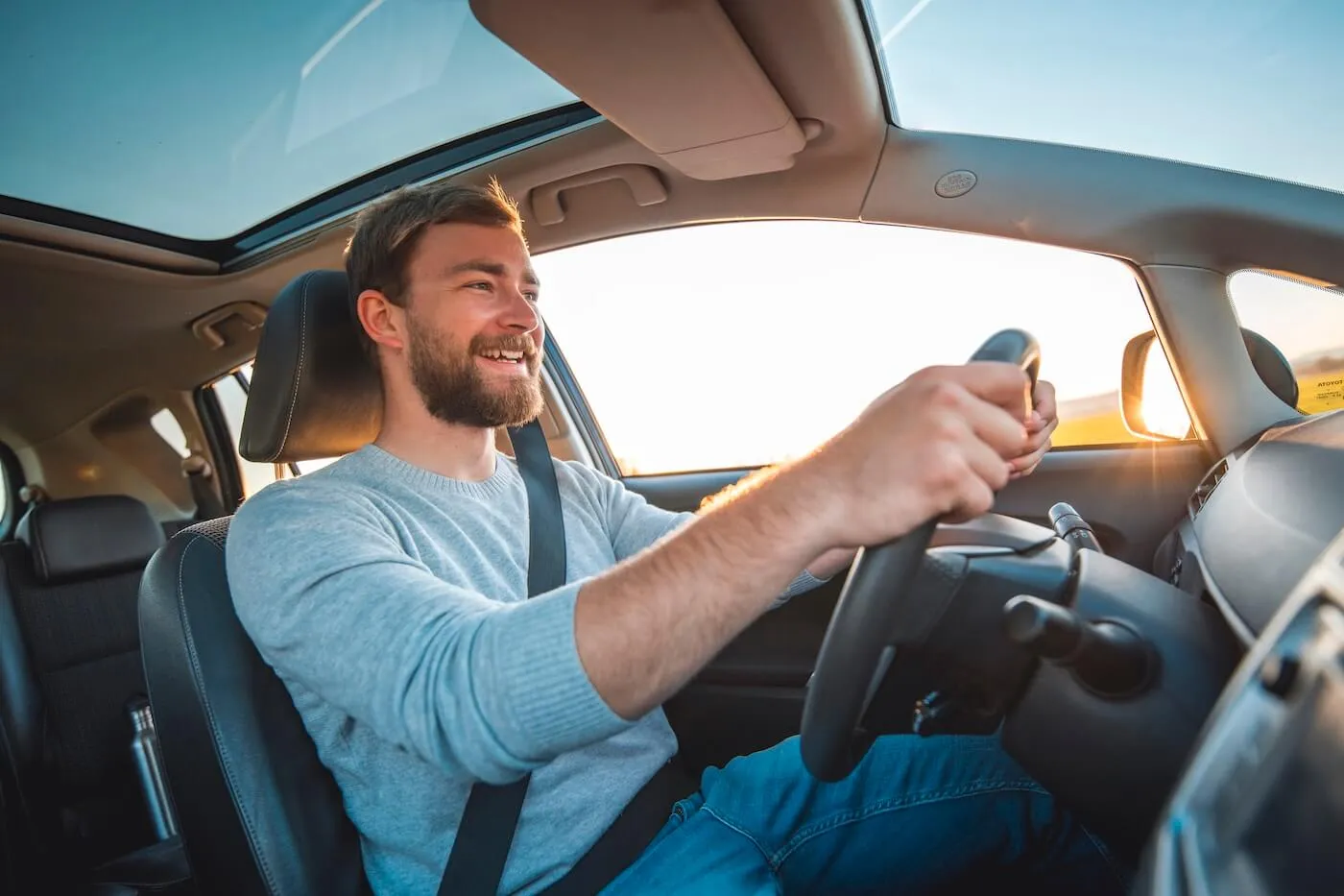 Smiling man driving a car at sunset