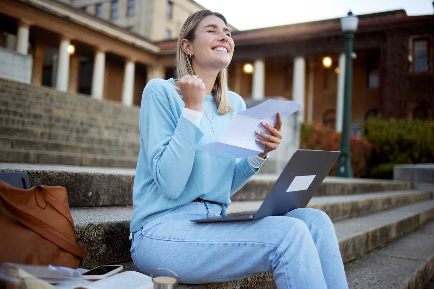 Student reading her financial aid award letter on the steps outside a school building.