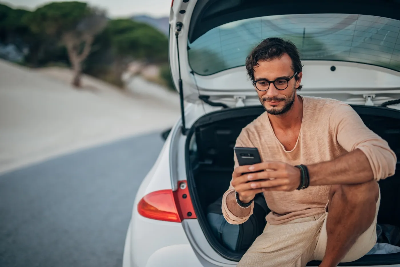 A man sitting in car trunk, using smart phone.