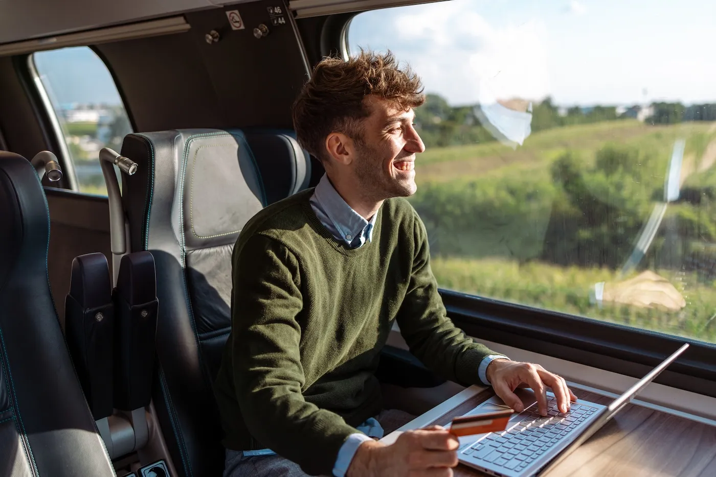 Photo of a young man traveling by train, smiling and looking out the window.