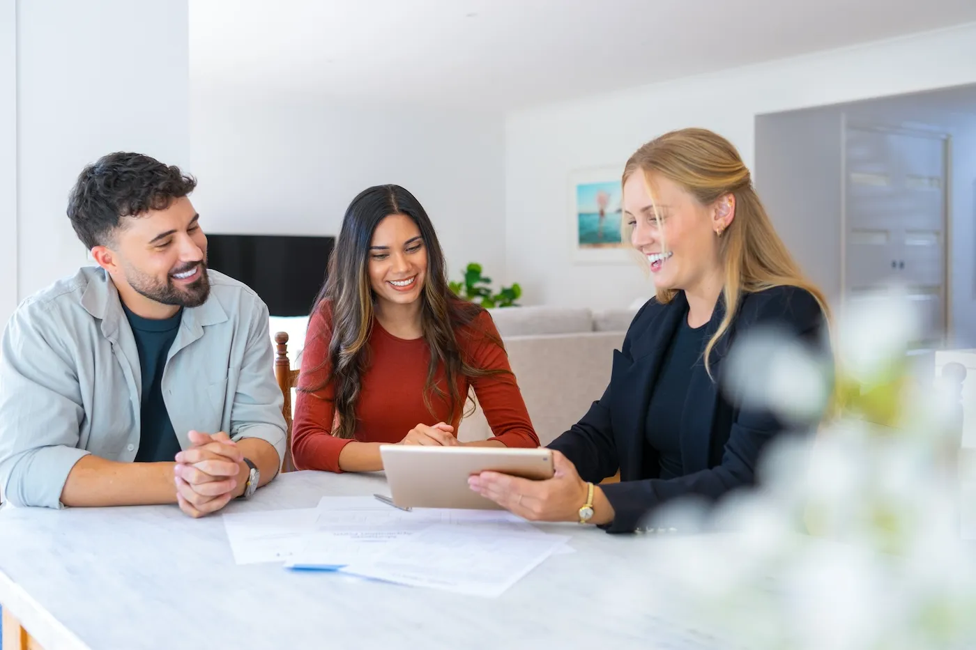 A real estate agent with a couple looking through documents. The agent is holding a digital tablet.