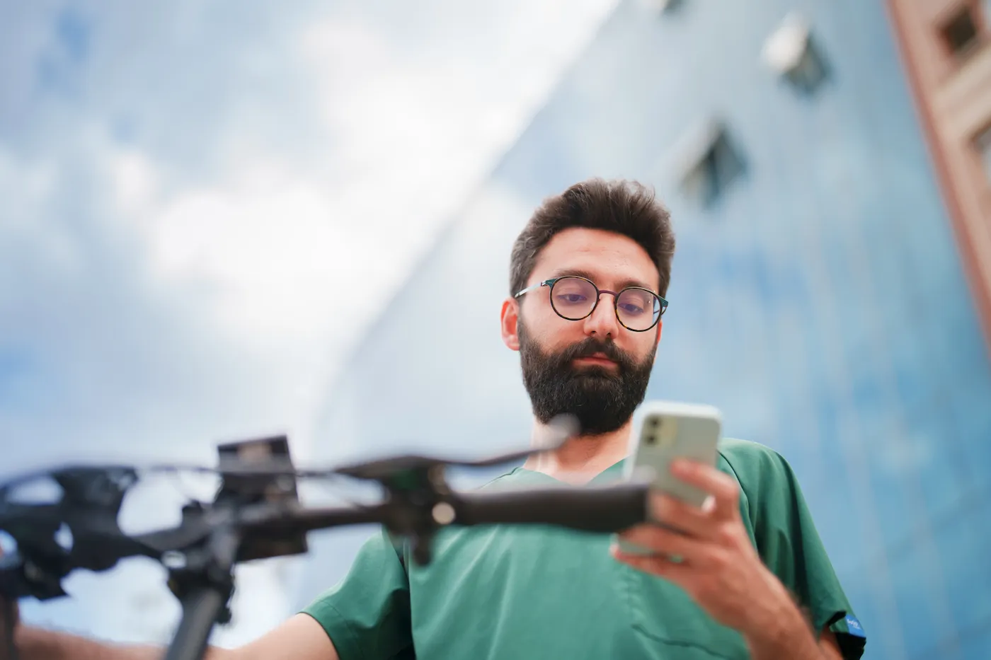 A man checking his phone outside while standing next to his bicycle.