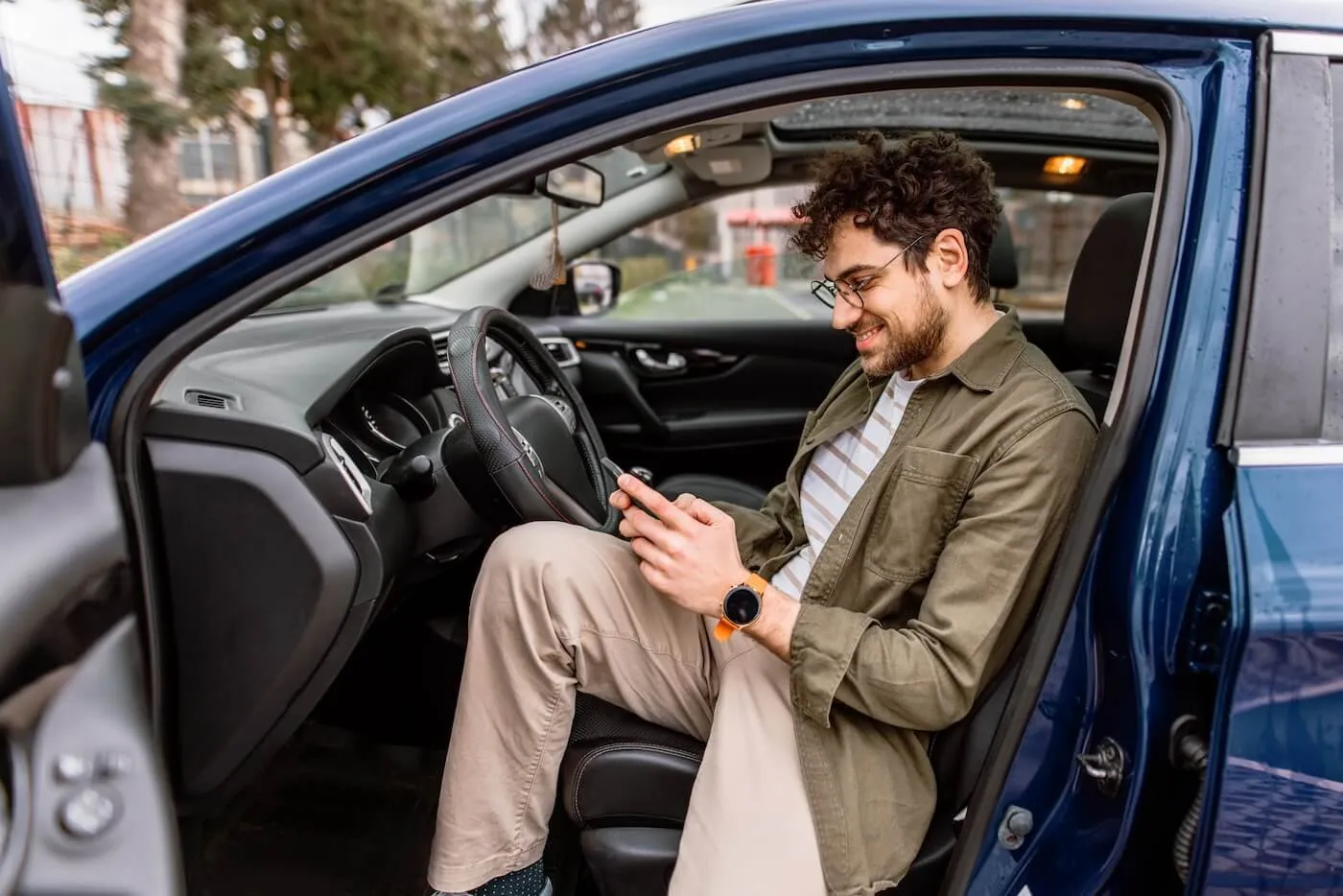 Smiling man using his smartphone while sitting in the parked car