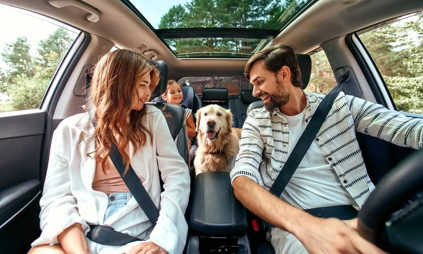 Happy family of three in the car with their dog