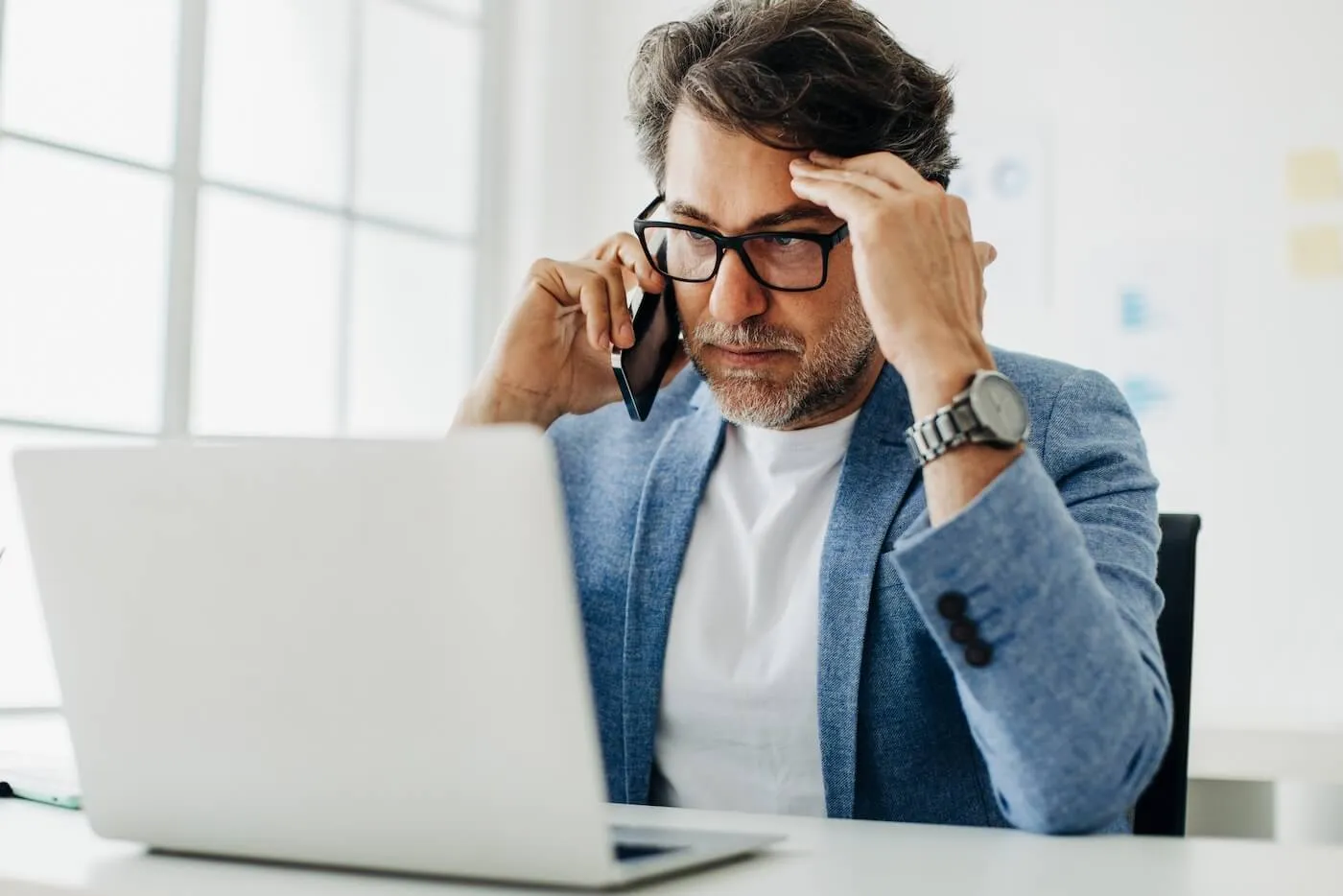 Concerned mature man is making a phone call while looking at the laptop screen