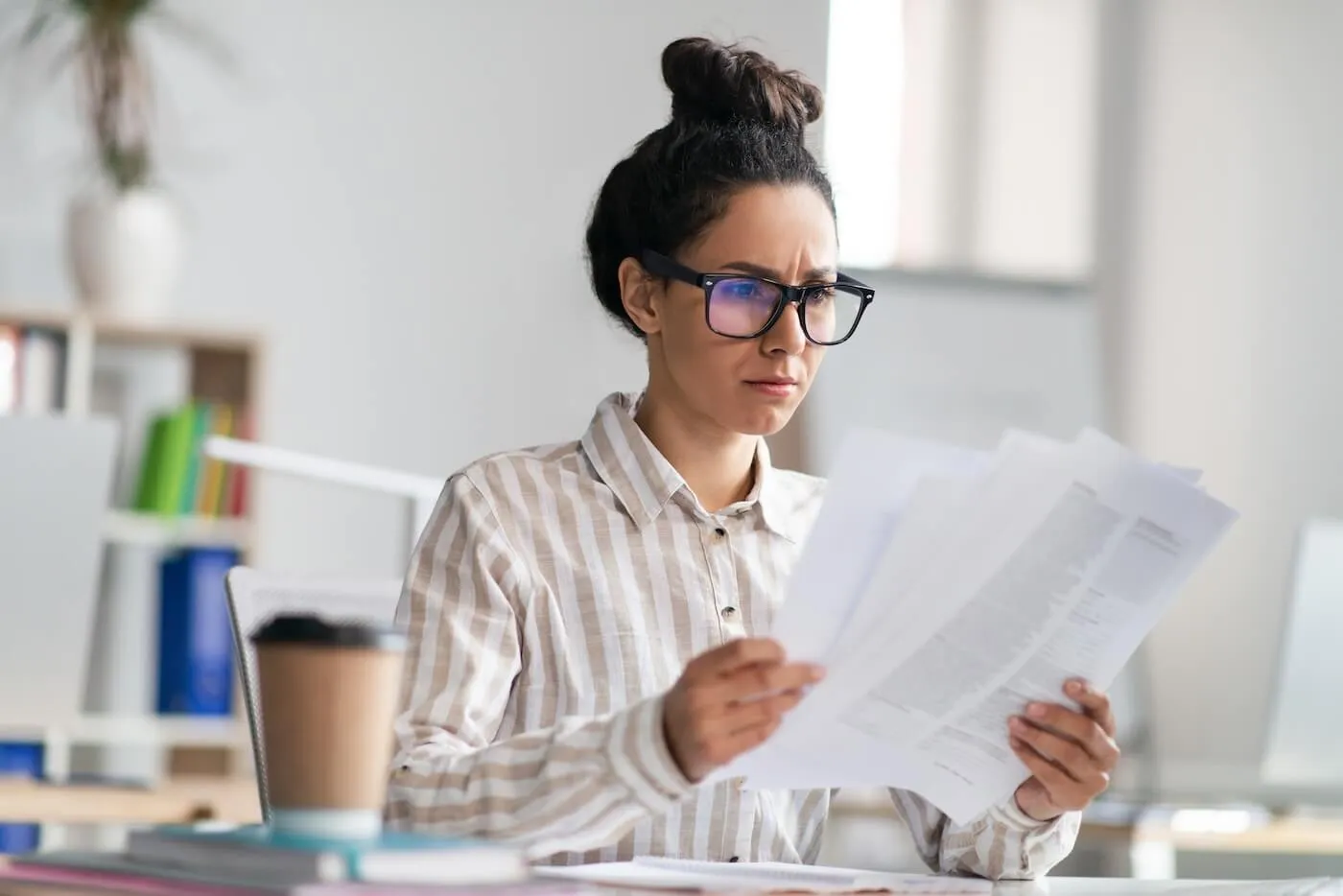 A focused woman in glasses reviewing the documents while having a coffee