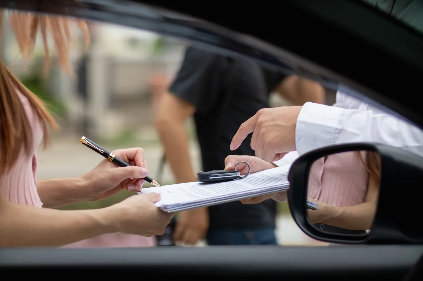 Insurance agents meet with customers, going over paperwork by a car.