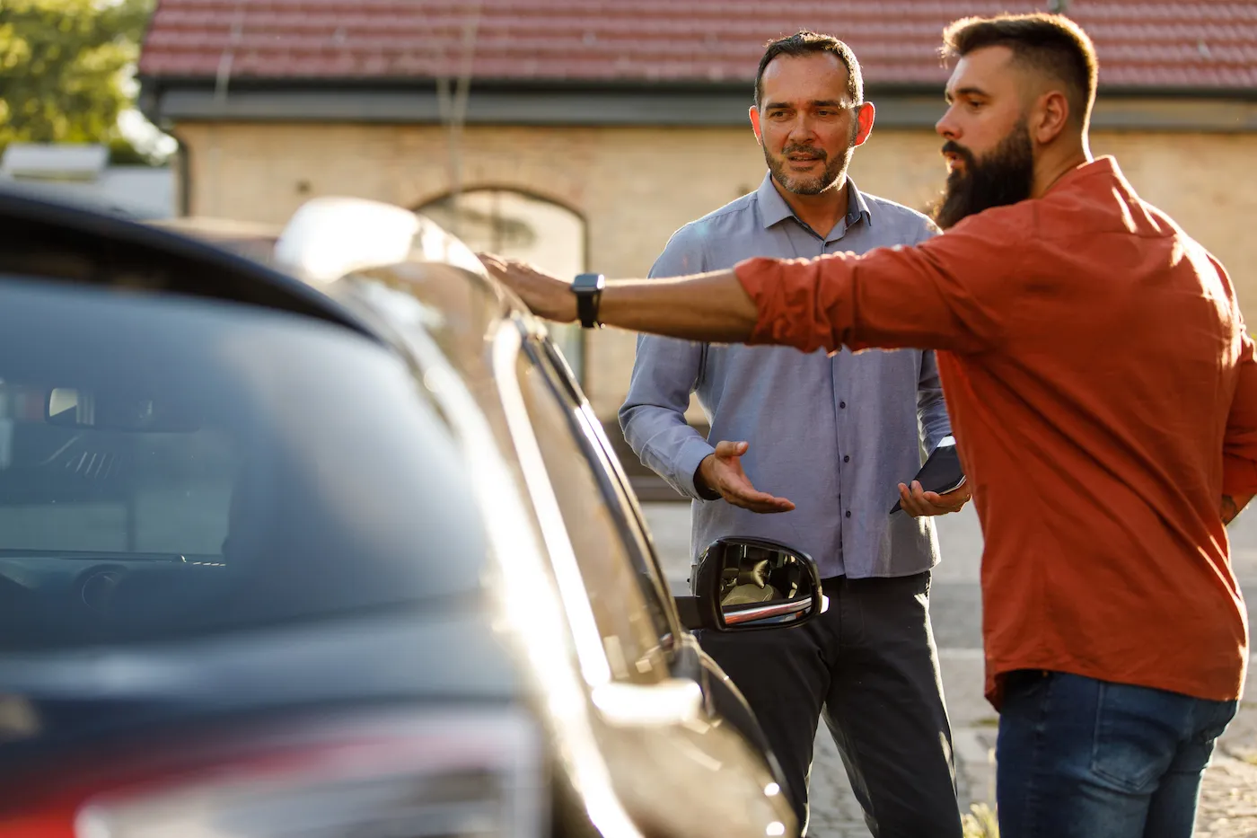 Copy space shot of mid adult salesman showing a car to a customer, sharing performances while inspecting the vehicle together.