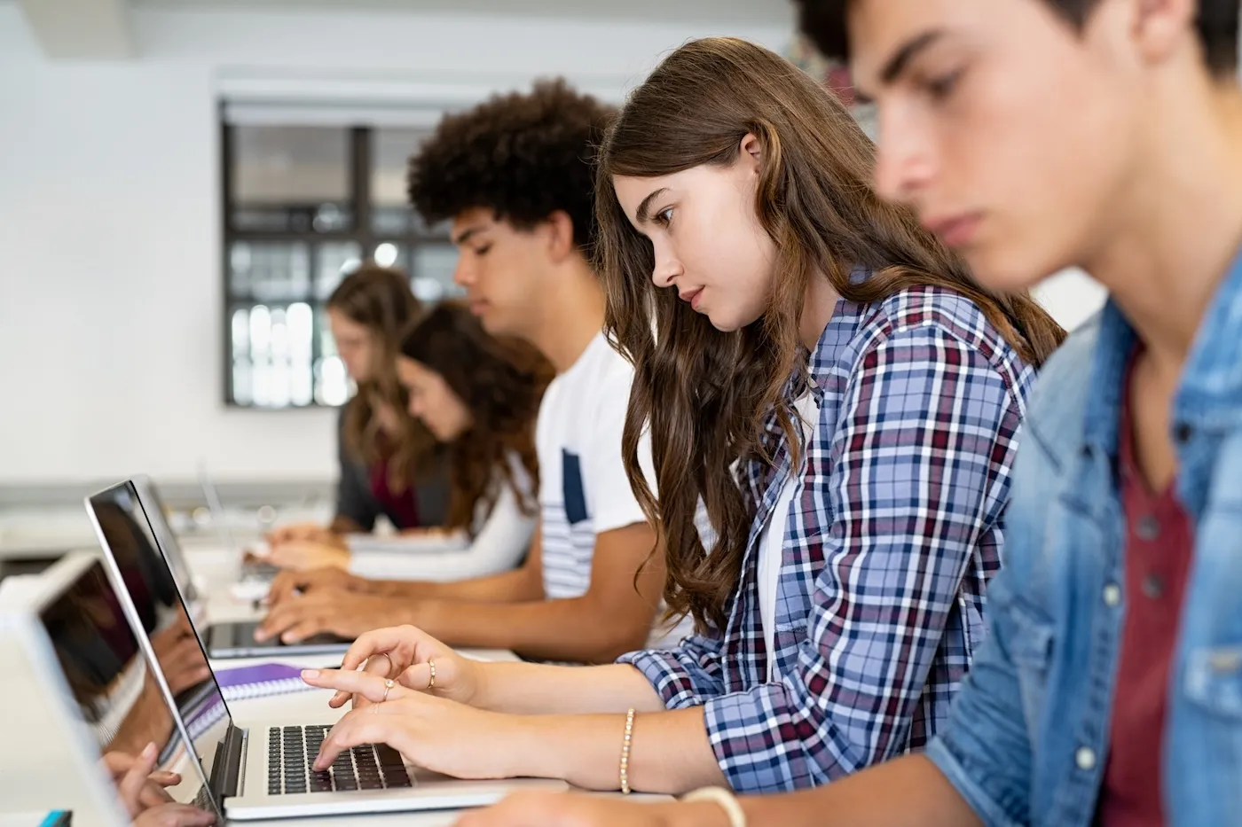 College students sitting in a classroom studying on laptop during class.