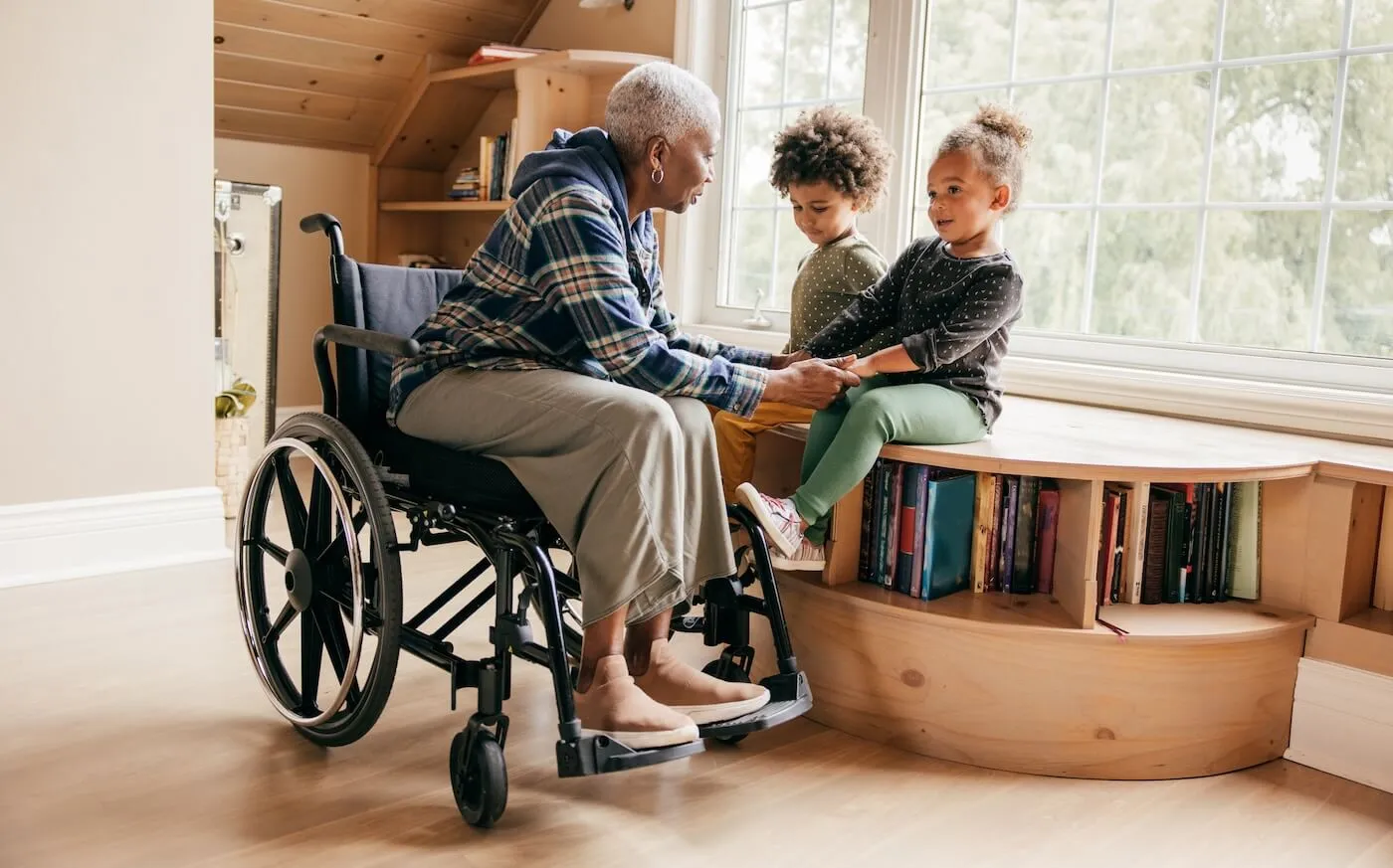 Senior woman on a wheelchair holding hands with her young grand children